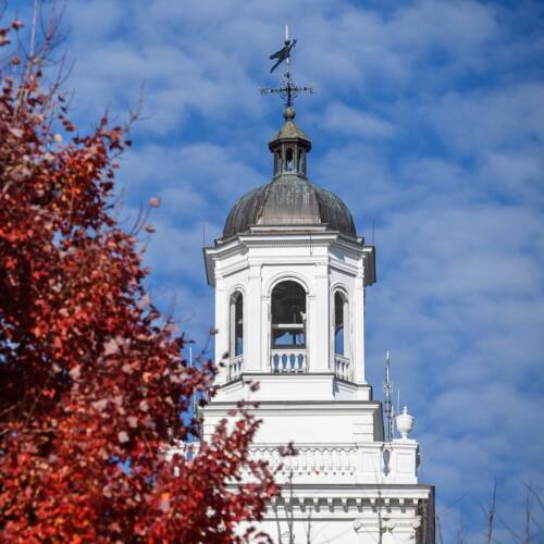 Gilman tower against a blue sky, next to red foliage