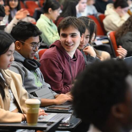 Students in a crowded lecture hall sit with laptops open